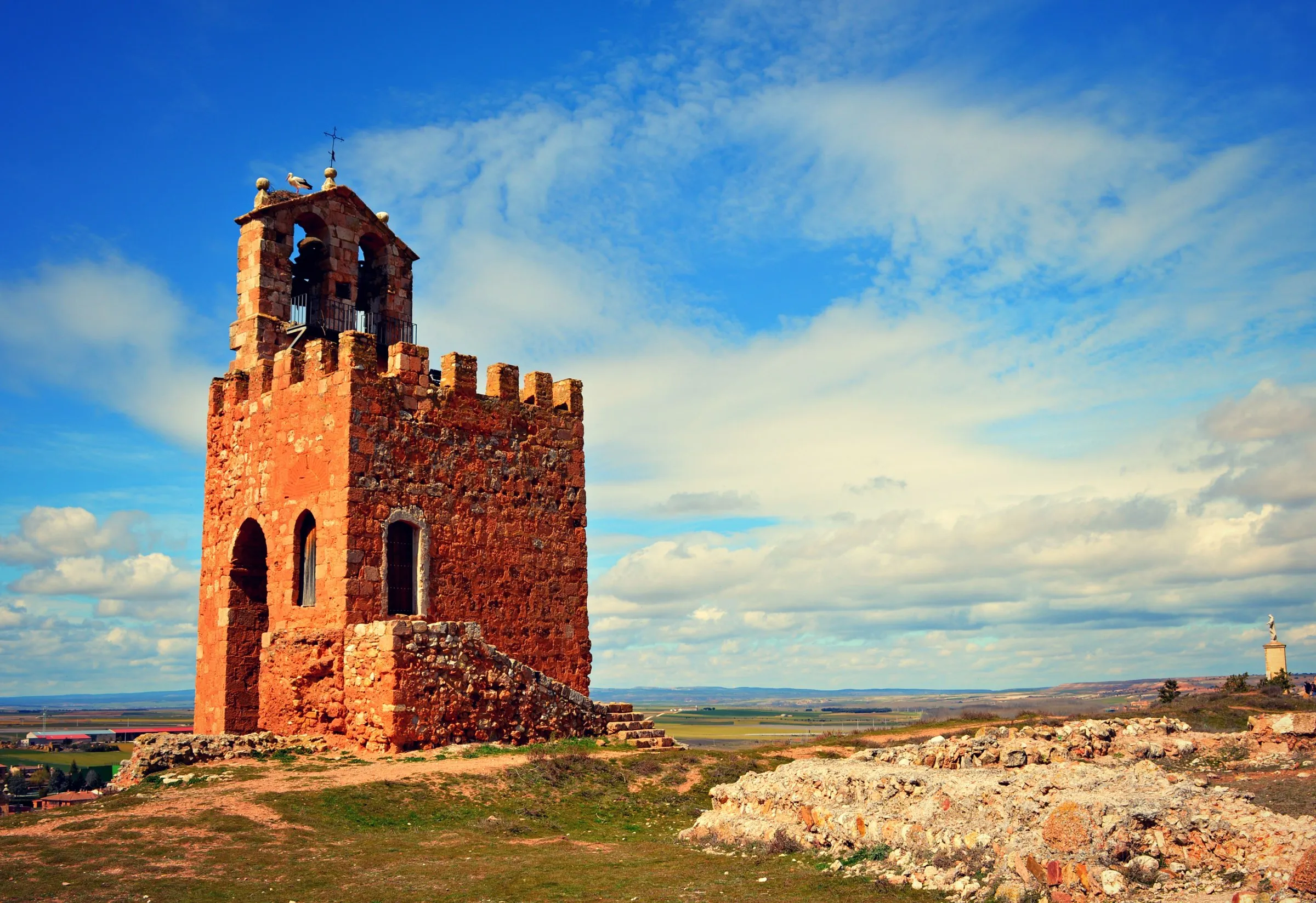 La Torre Martina del castillo de Ayllón, de piedra rojiza y almenada, con una espadaña de campanas encima, sobre el cerro y con la llanura al fondo
