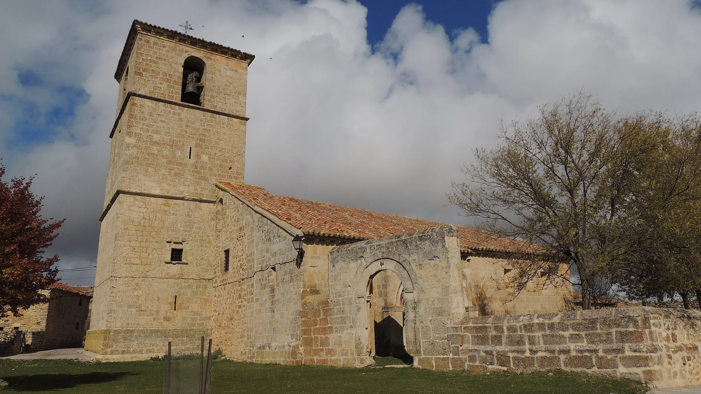 La iglesia de San Pedro de Villacadima vista desde fuera, con su torre de piedra, bajo un cielo de nubes