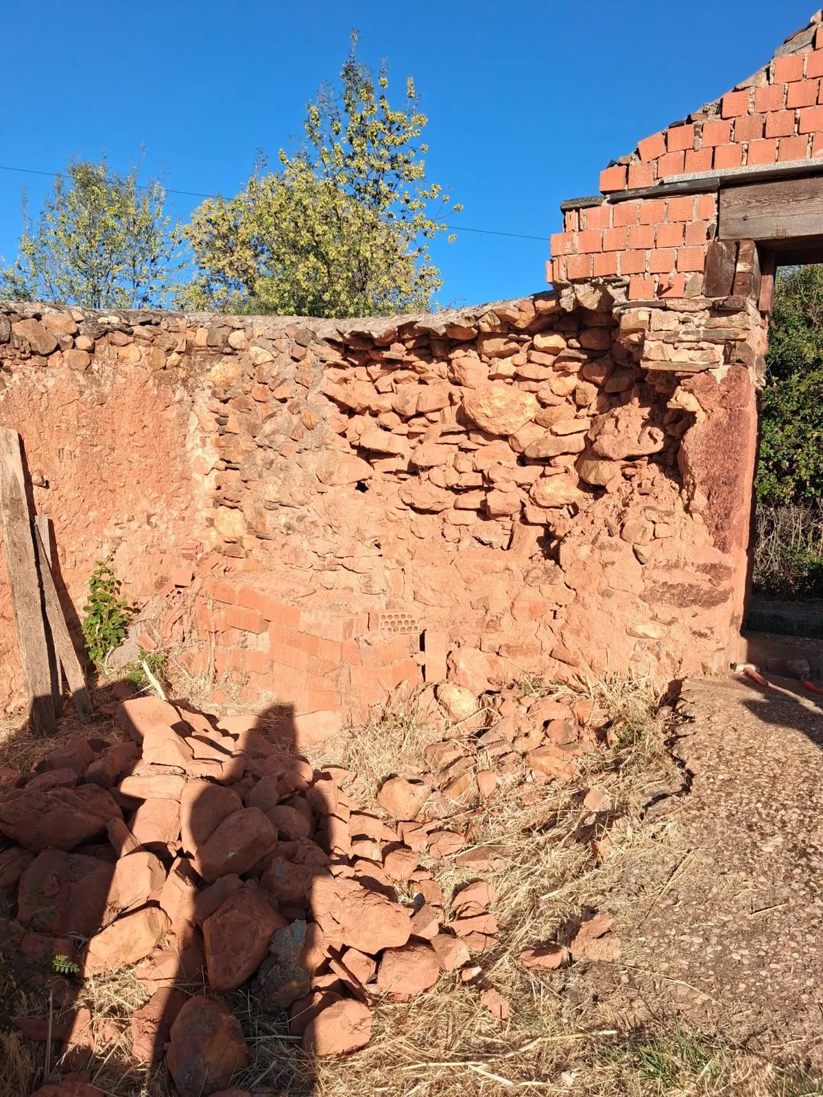Piedra roja apilada al pie de la tapia del cementerio, junto a la portada de ladrillo