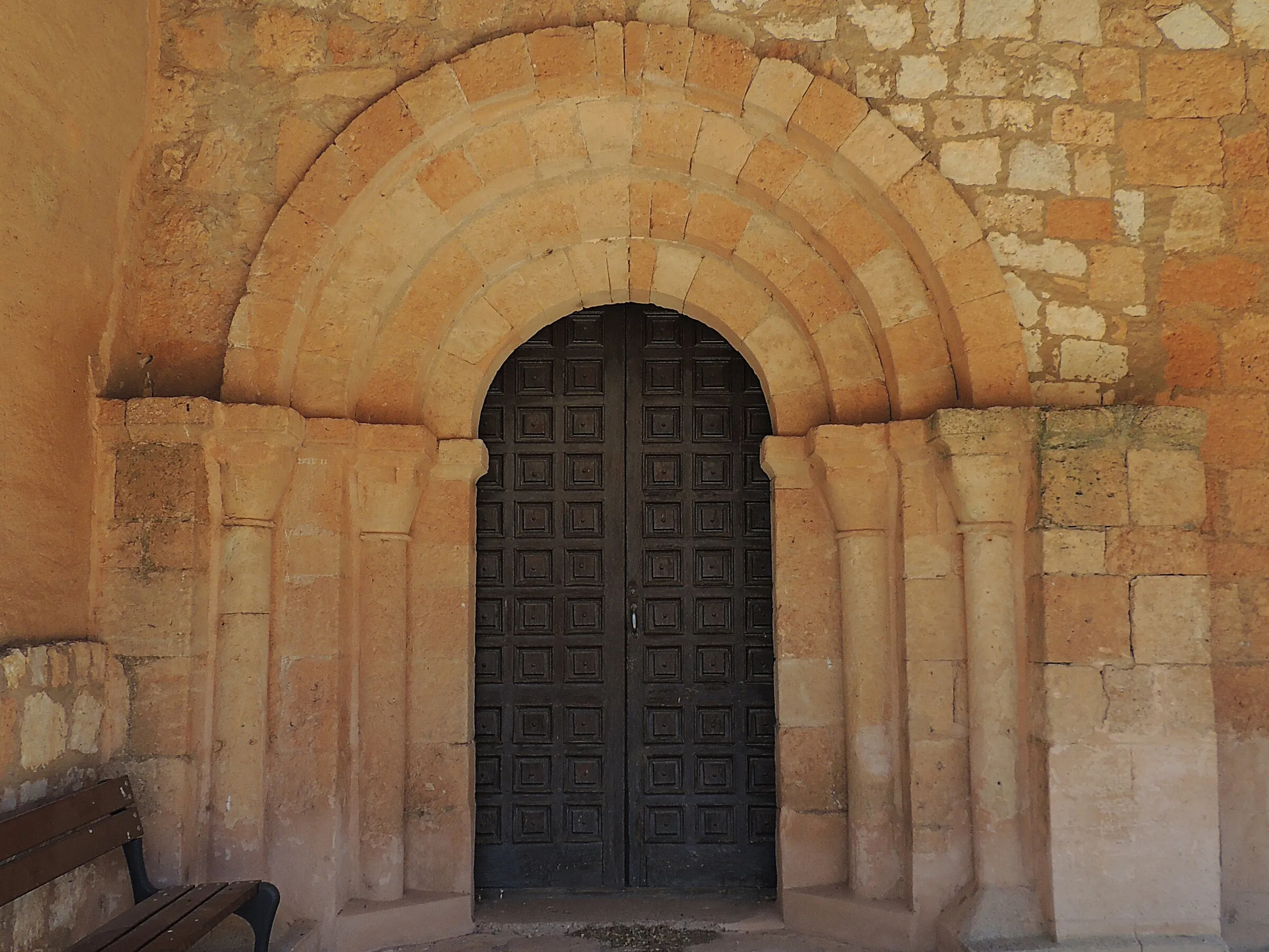 La portada románica de San Juan Bautista de Mazagatos: cuatro arquivoltas lisas de medio punto sobre columnas y jambas, una puerta de madera de cuarterones y el techo de madera del pórtico