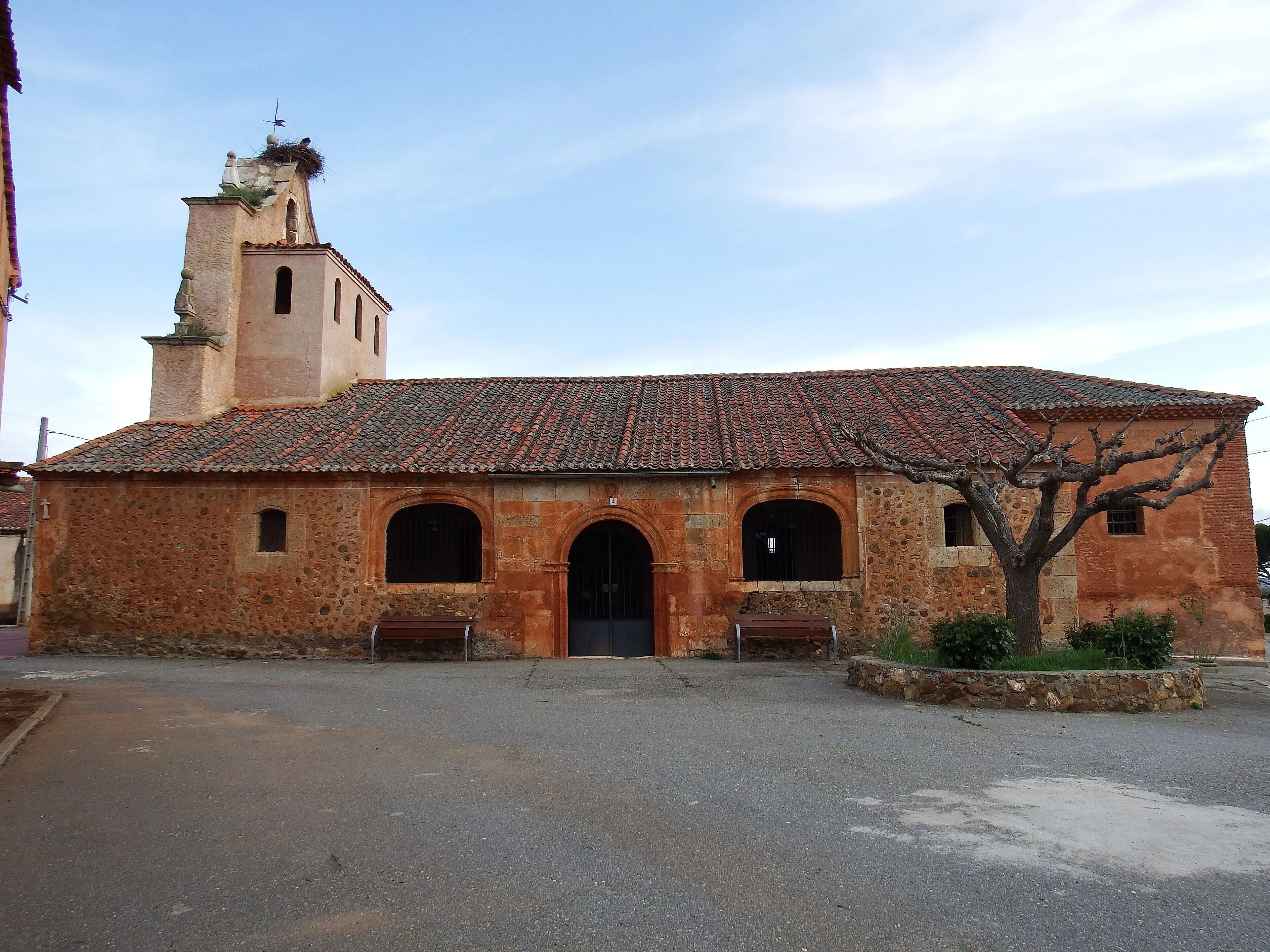 La iglesia de San Juan Degollado de Ribota: la nave de mampostería con el pórtico cerrado de arcos y la torre, con un nido de cigüeña