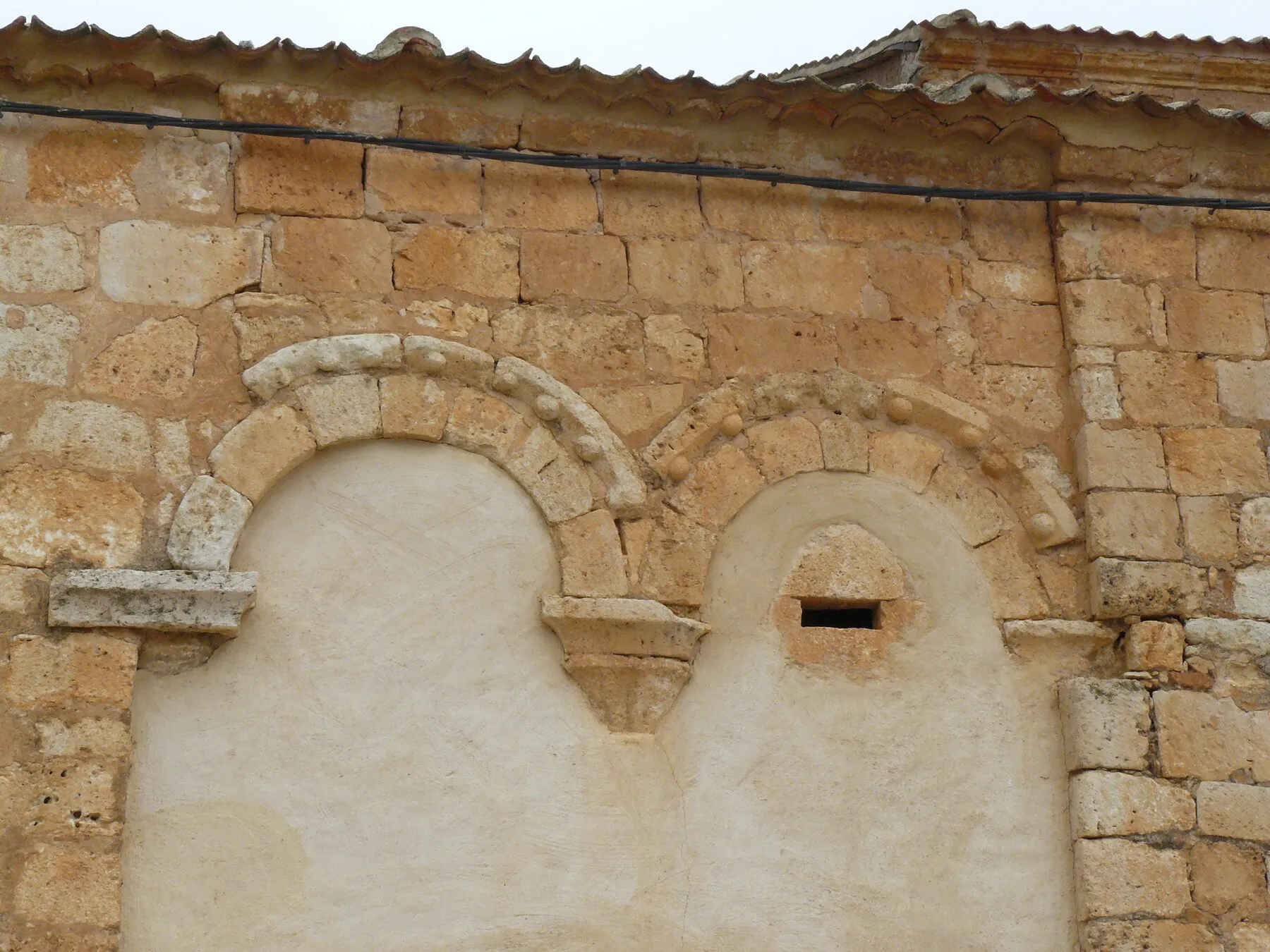 Muro de sillería de la iglesia con dos arcos de medio punto tapiados y enlucidos