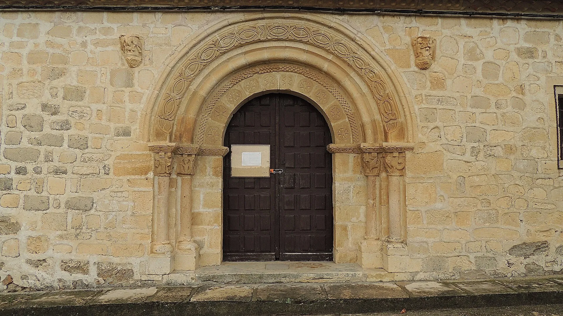 La portada románica del muro norte: arco de medio punto con flores de seis pétalos en las dovelas, dos arquivoltas y capiteles pareados