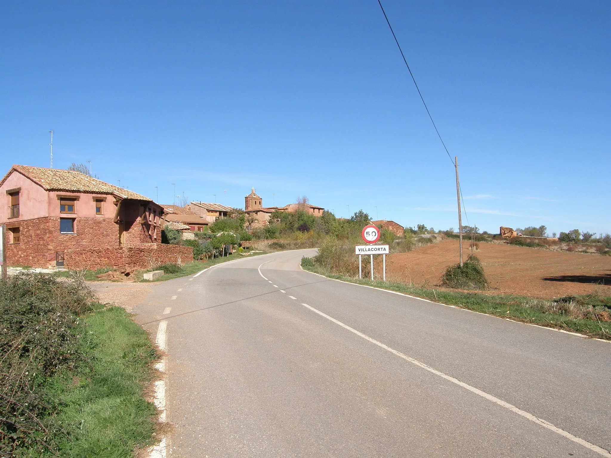 La carretera llegando a Villacorta, con el caserío rojo y la torre de la iglesia