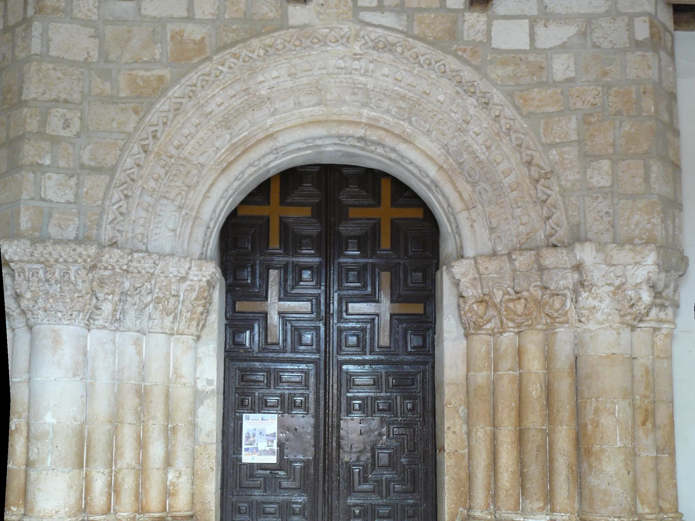 La portada románica de San Miguel Arcángel de Languilla: cuatro arquivoltas decoradas sobre grupos de columnas con capiteles tallados y una puerta de madera de cuarterones con cruces