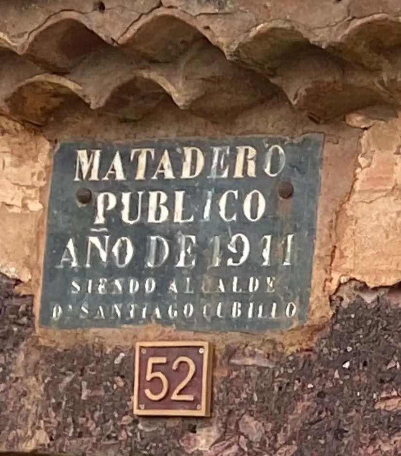 Placa de chapa oscura con letras blancas, bajo un alero de teja, que dice «Matadero público, año de 1911, siendo alcalde D. Santiago Cubillo»
