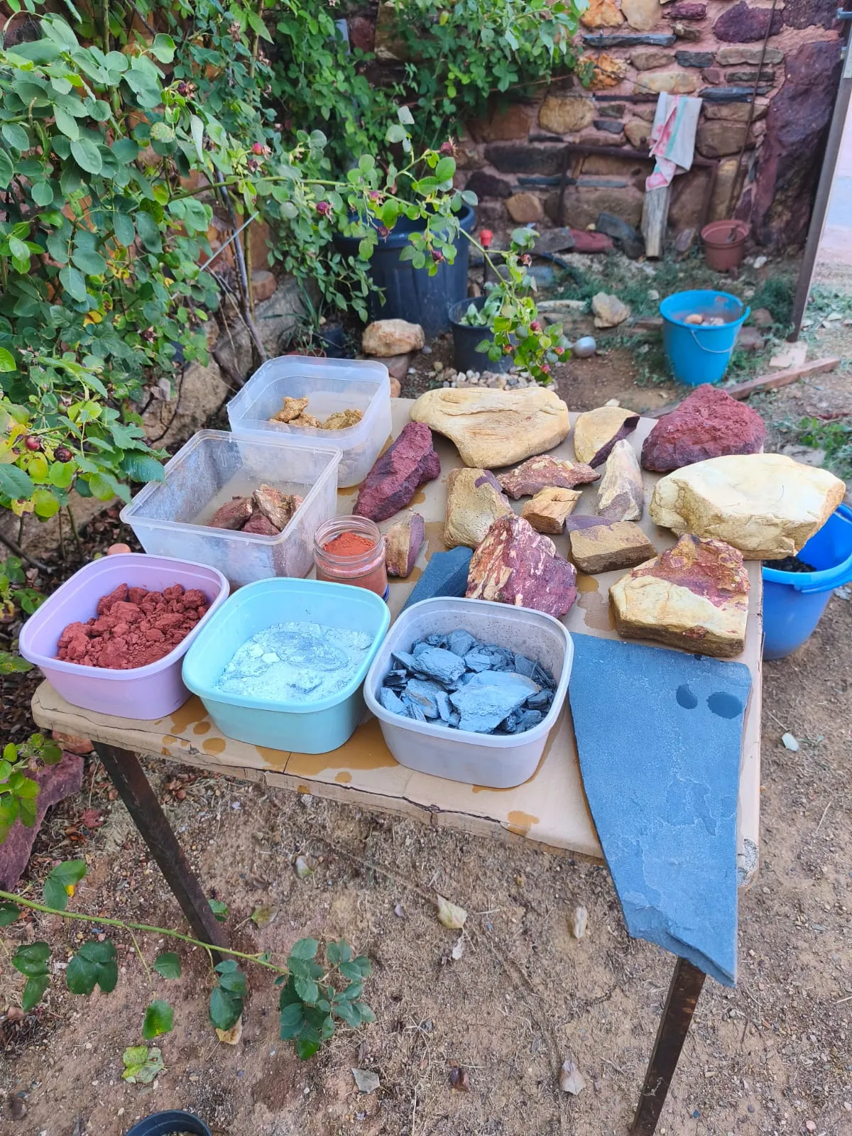 Barreños con el material molido: rojo en polvo, escamas de pizarra y un blanco azulado, y un tarro de cristal con el pigmento rojo ya preparado