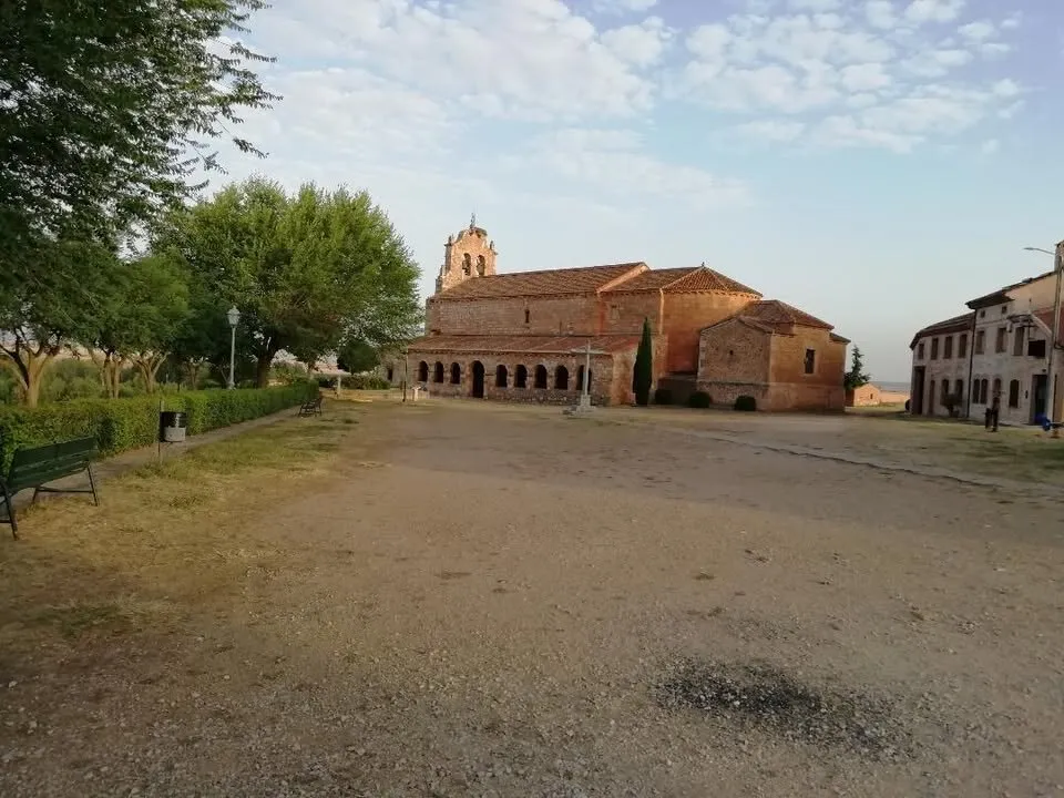 La plaza de tierra con bancos y árboles y, al fondo, la iglesia de la Natividad con su pórtico y la espadaña