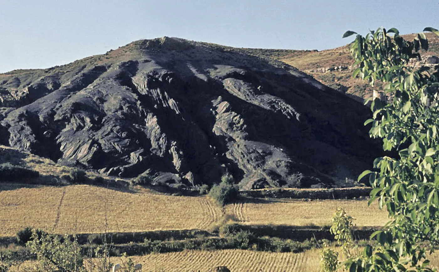 Un cerro de pizarra oscura con las capas dobladas y retorcidas, sobre campos de labor, en Santibáñez de Ayllón en 1974
