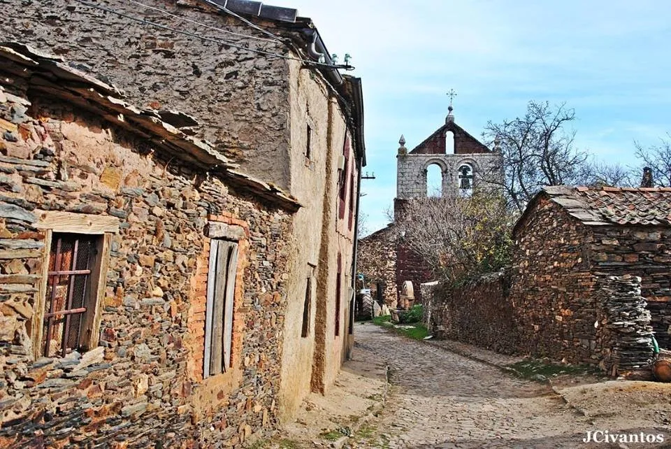 Calle de Serracín entre casas de pizarra, con la espadaña de la iglesia al fondo